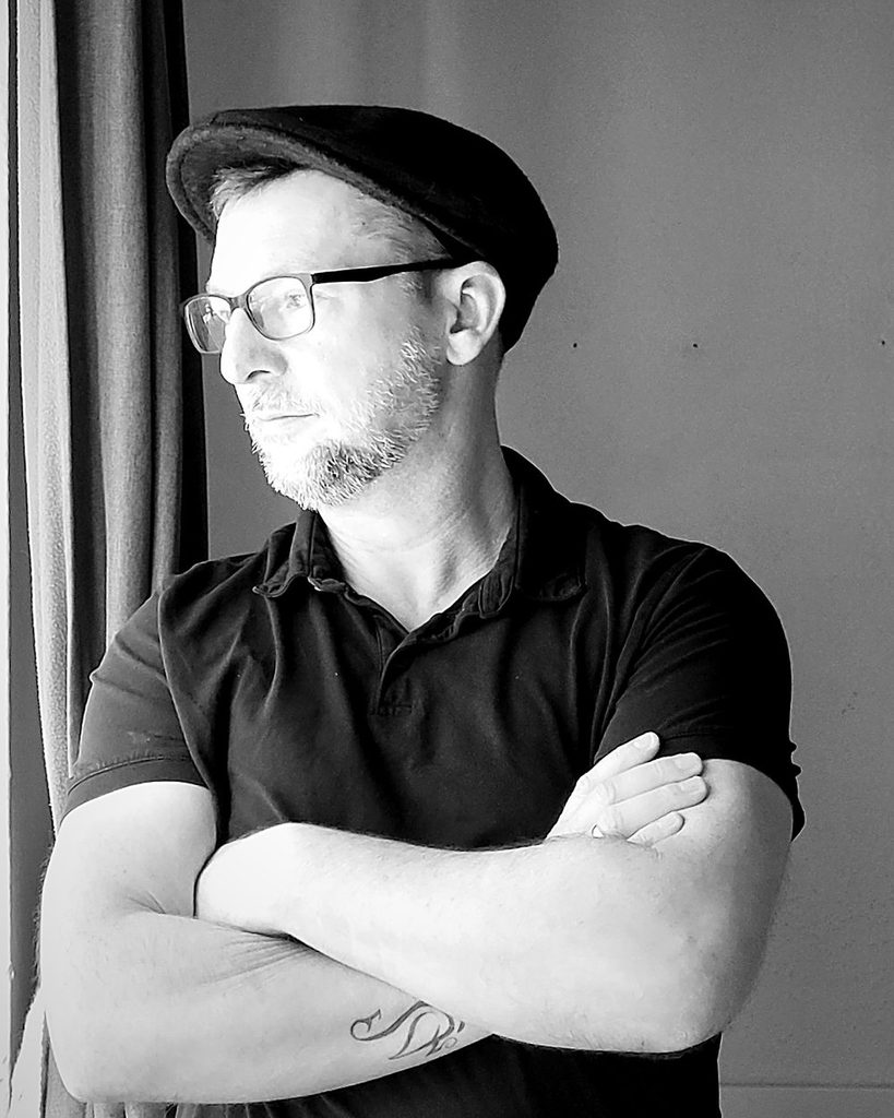 Dr. Marcus Reiß, author of Grammar of Magic, wearing a flat cap (black-and-white portrait)